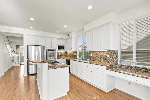 a kitchen with stainless steel appliances kitchen island granite countertop a refrigerator stove oven and white cabinets with wooden floor