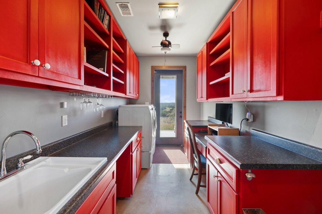 1292 Upper Turtle Creek Road Kerrville, TX 78028 - Photo 12 of 40 Butlers pantry with red cabinetry, reddish brown cabinets, dark countertops, open shelves, and built in desk with washer and dryer