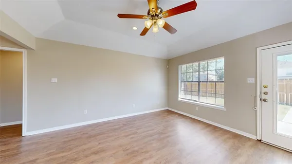 an empty room with wooden floor fan and windows