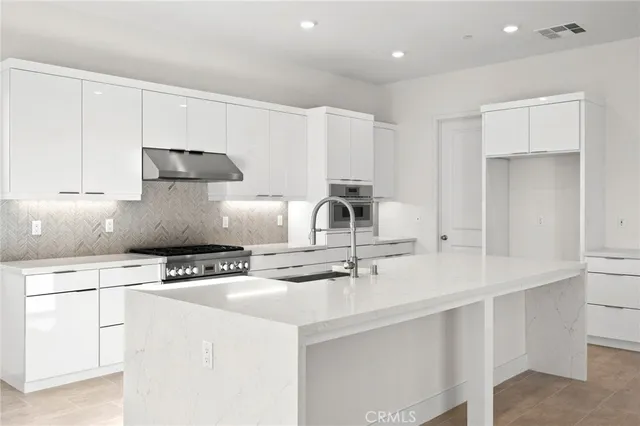 a kitchen with kitchen island granite countertop a sink a stove and white cabinets