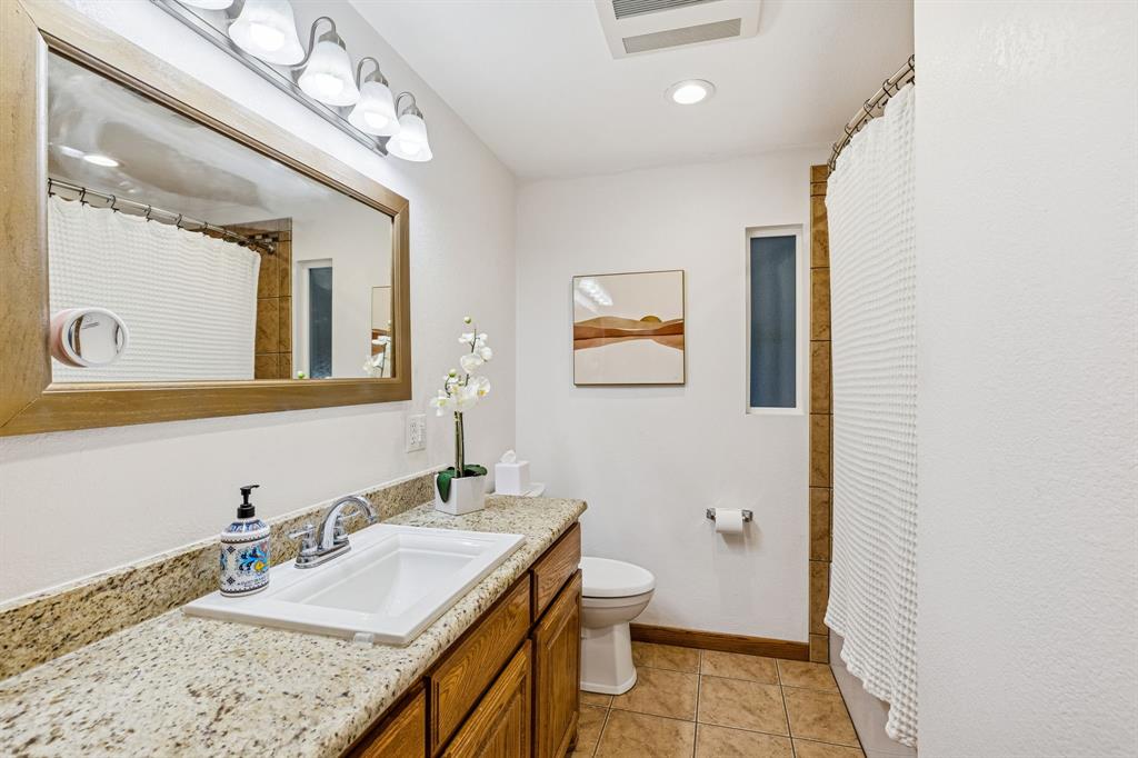 1012 Cowling Road Sanger, TX 76266 - Photo 19 of 40 a bathroom with a granite countertop sink mirror vanity and toilet