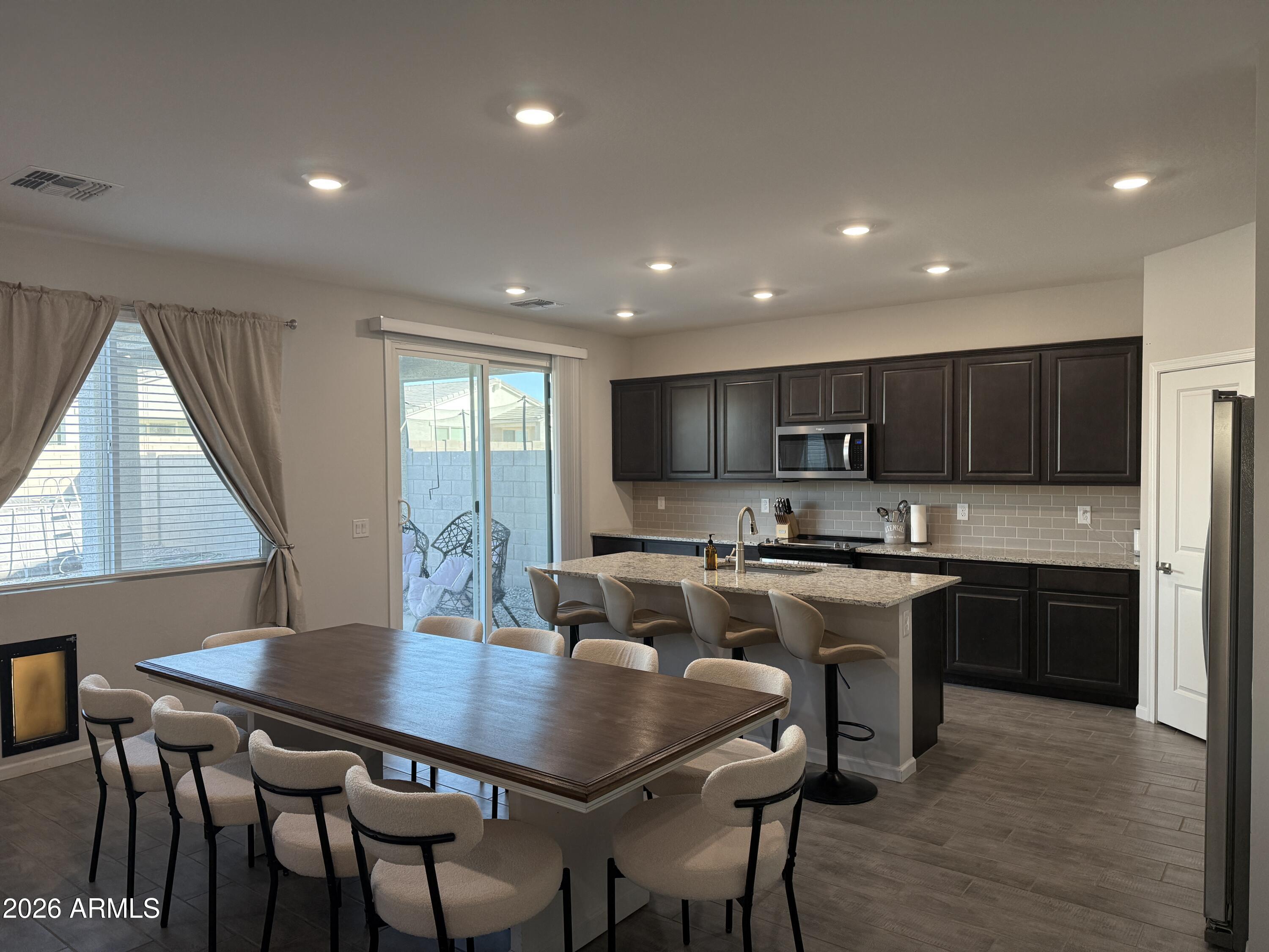 18140 West Daley Lane Surprise, AZ 85387 - Photo 2 of 23 a kitchen with stainless steel appliances a dining table chairs stove refrigerator and microwave