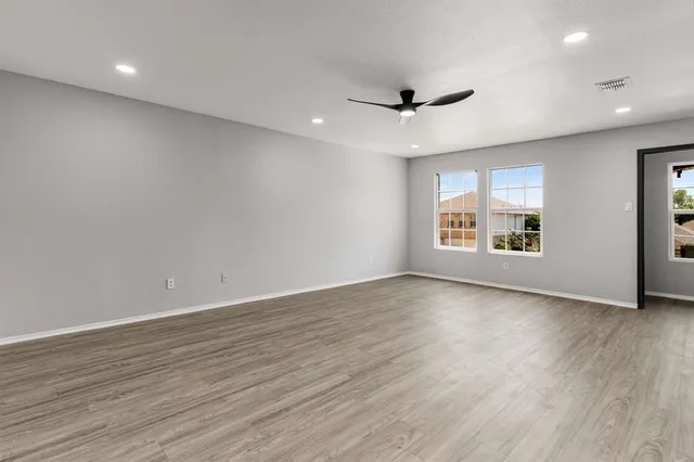 an empty room with wooden floor ceiling fan and windows