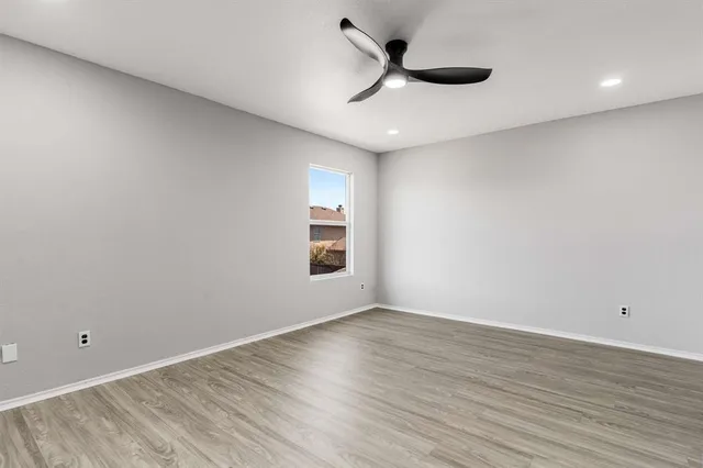 a view of an empty room with wooden floor and a ceiling fan