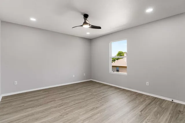 an empty room with wooden floor chandelier fan and windows