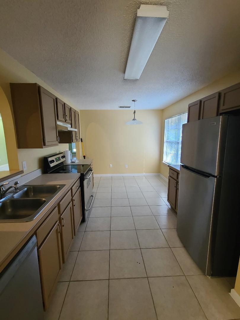 11996 Swooping Willow Road Jacksonville, FL 32223 - Photo 5 of 13 Kitchen with stainless steel appliances, hanging light fixtures, a textured ceiling, light tile patterned flooring, and light countertops