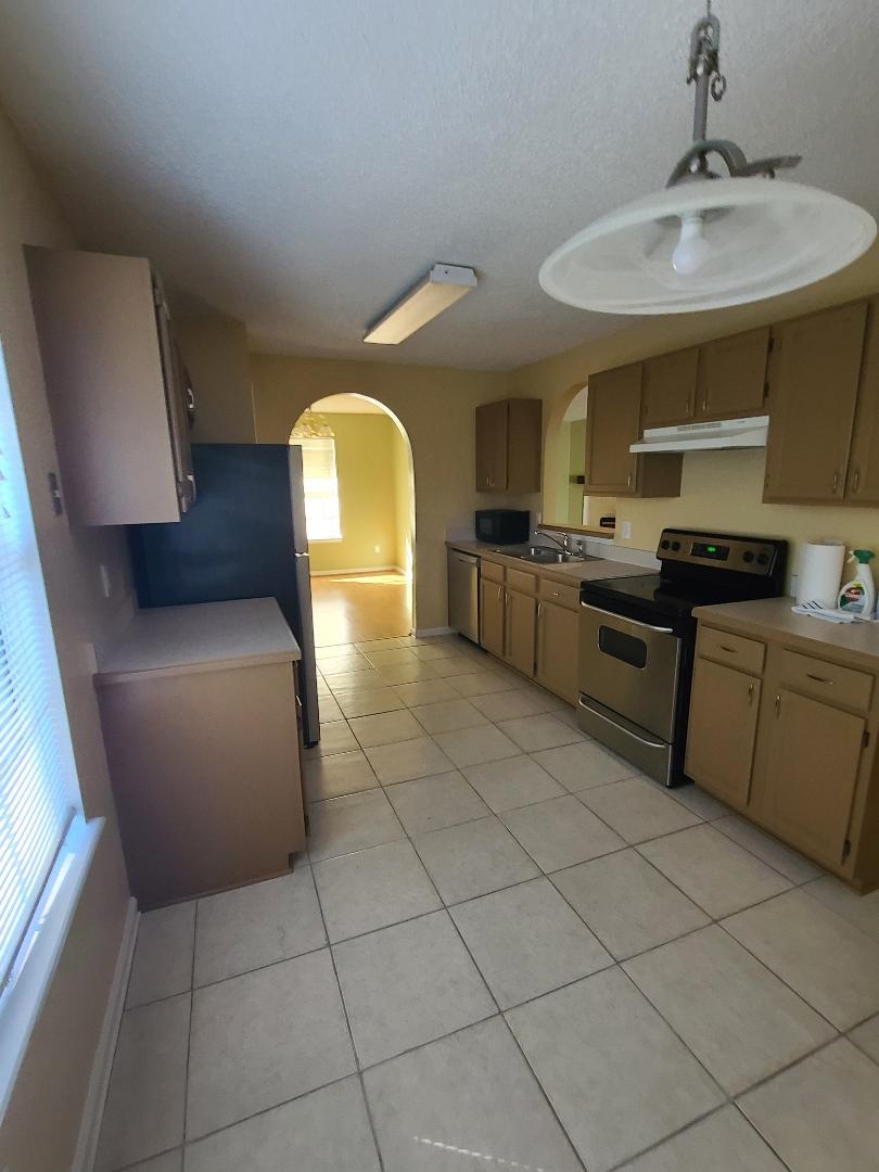11996 Swooping Willow Road Jacksonville, FL 32223 - Photo 6 of 13 Kitchen with stainless steel appliances, arched walkways, light countertops, light tile patterned floors, and under cabinet range hood