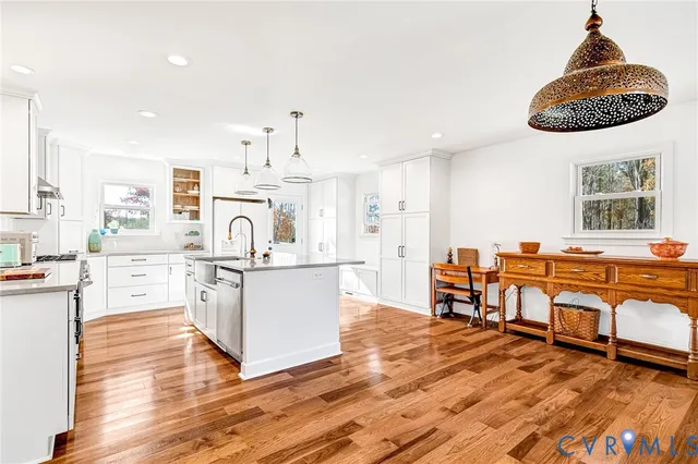 a living room with stainless steel appliances kitchen island granite countertop a stove a sink dishwasher and white cabinets with wooden floor