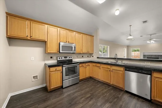 a kitchen with stainless steel appliances granite countertop white cabinets a sink a stove a refrigerator and microwave with wooden floor