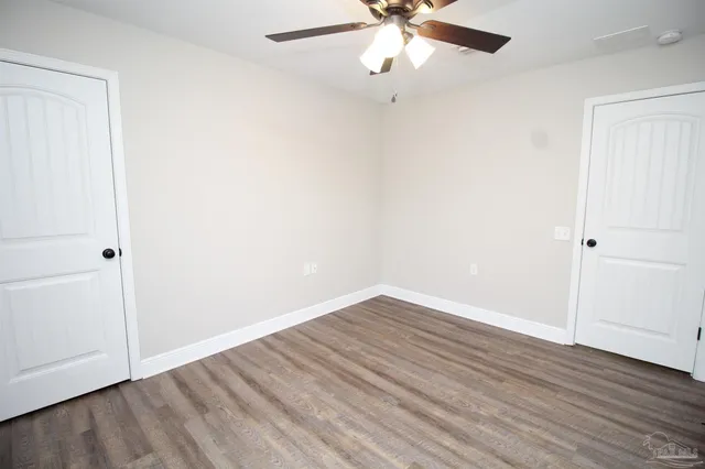 an empty room with wooden floor fan and windows
