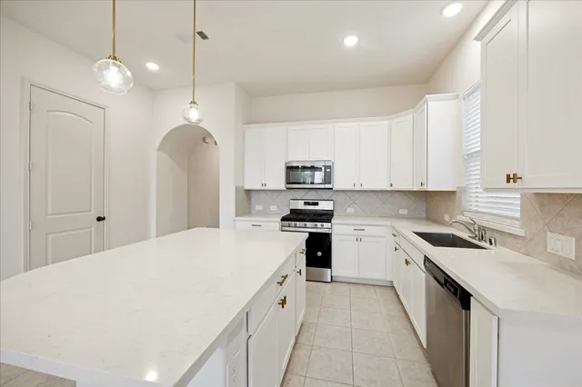 a kitchen with stainless steel appliances kitchen island granite countertop a refrigerator a sink dishwasher a stove and white cabinets with wooden floor