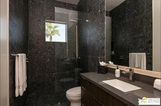 a bathroom with a granite countertop sink a toilet a mirror and shower