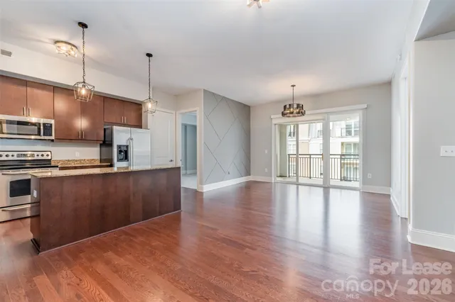 a open kitchen with stainless steel appliances granite countertop a stove top oven a sink with wooden floors and a chandelier