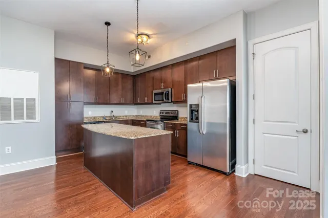 a kitchen with stainless steel appliances granite countertop a refrigerator a sink a stove and a wooden floors