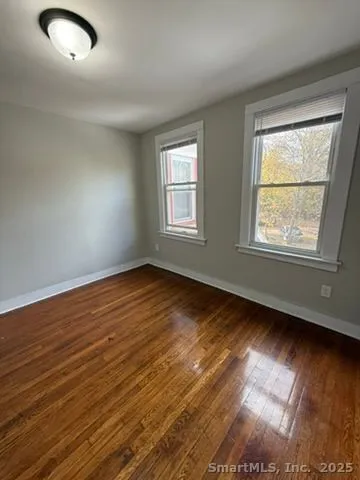 a view of an empty room with wooden floor and a window
