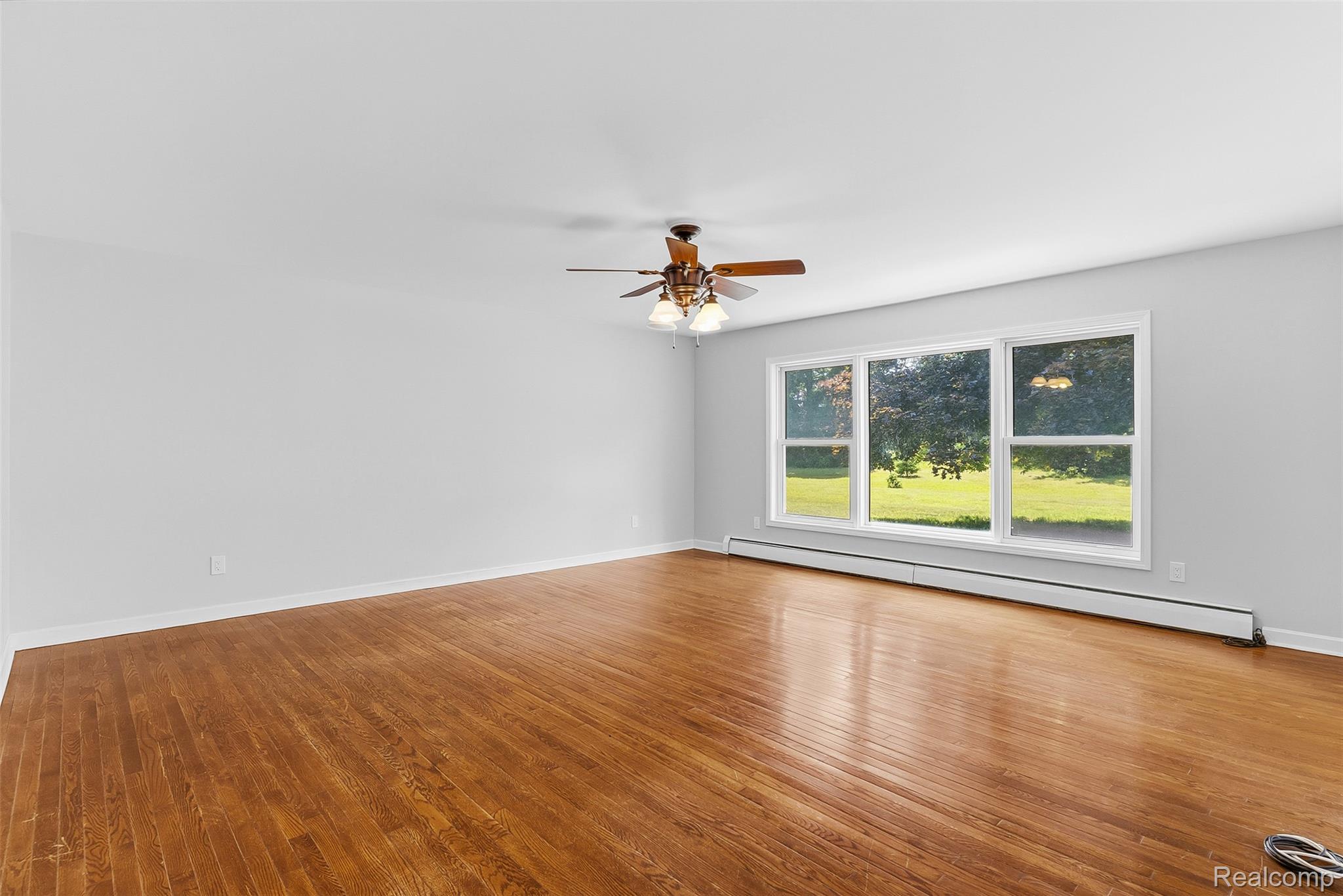 9200 Hickory Ridge Road Holly, MI 48442 - Photo 9 of 33 Spacious room featuring wood-finish flooring, a contemporary ceiling fan with lighting, and a large three-panel window overlooking a green landscape
