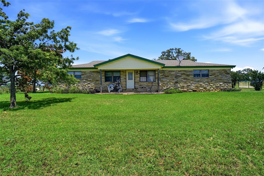2186 Gilliland Road Springtown, TX 76082 - Photo 12 of 25 Ranch-style exterior featuring stone facade, a covered front porch, and a lush green lawn