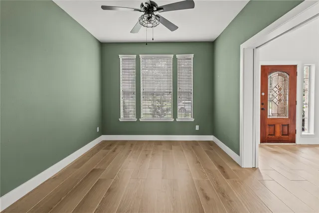 an empty room with wooden floor chandelier fan and windows