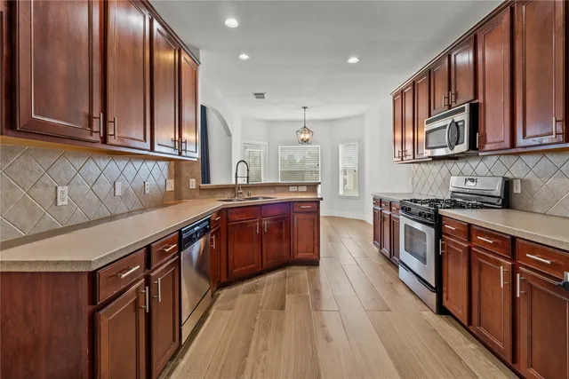 a kitchen with stainless steel appliances granite countertop a stove a sink dishwasher and wooden cabinets with wooden floor