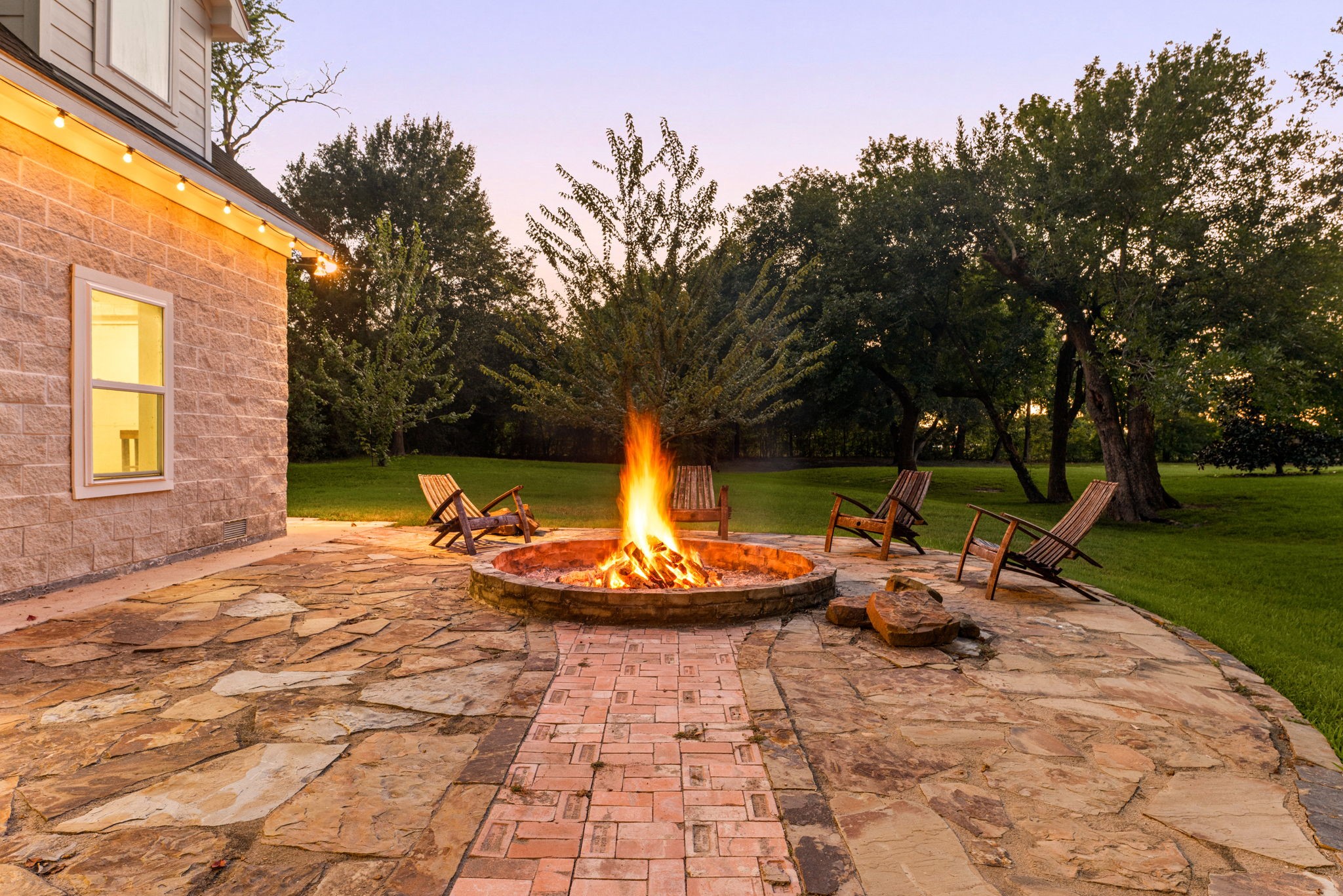 6039 Franz Road Katy, TX 77493 - Photo 44 of 49 As dusk falls, the custom brick-and-stone fire pit glows beside the stone-clad barn, surrounded by string lights, an intimate gathering spot tucked beneath mature trees.