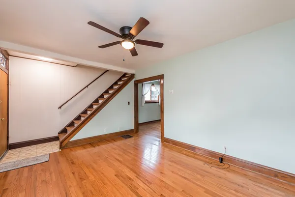 a view of an empty room with wooden floor and a ceiling fan
