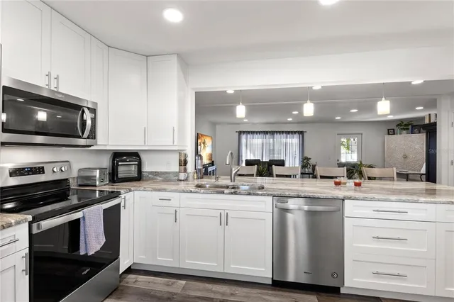 a kitchen with stainless steel appliances kitchen island granite countertop a stove top oven a sink and white cabinets