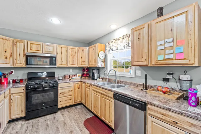 a kitchen with stainless steel appliances granite countertop a stove a sink dishwasher and white cabinets with wooden floor