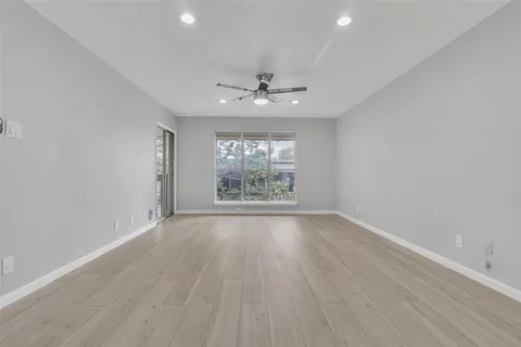 an empty room with wooden floor chandelier fan and windows