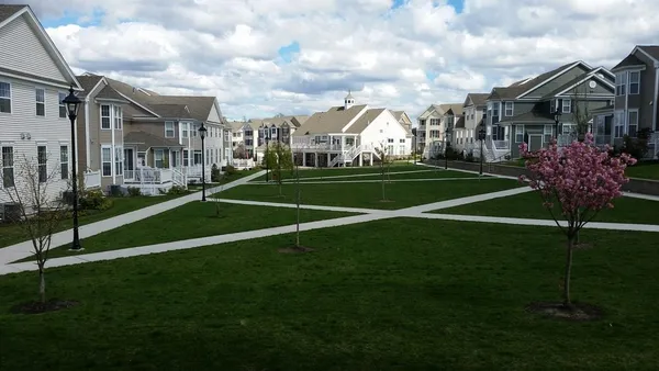 a view of a white house in front of a big yard with potted plants