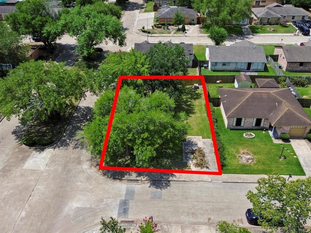 This aerial view of this residential neighborhood highlights the property for sale, outlined in red. The lot is surrounded by single-family homes with ample greenery and is located on a calm street with easy road access.
