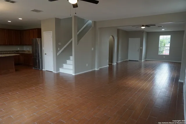 a view of an empty room with wooden floor kitchen view and a window