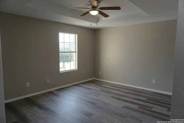 an empty room with wooden floor fan and windows