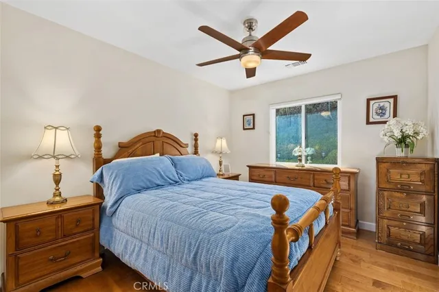 a bedroom with a bed a dresser and potted plants with the wooden floor