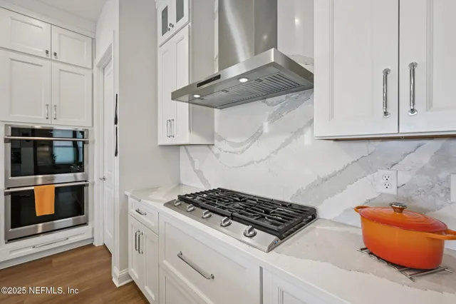 a kitchen that has a lot of white cabinets and stainless steel appliances
