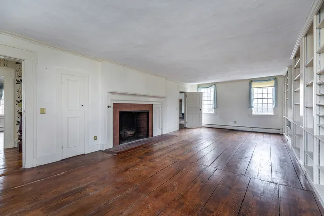 an empty room with wooden floor fireplace and windows