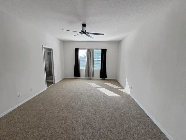 an empty room with chandelier fan and windows