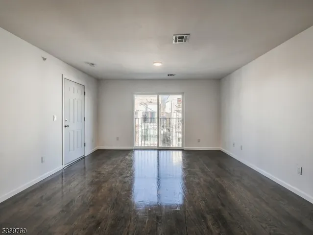 a view of an empty room with wooden floor and fan