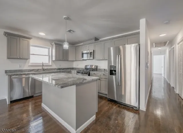 a kitchen with stainless steel appliances granite countertop a refrigerator a sink dishwasher a stove and white countertops with wooden floor