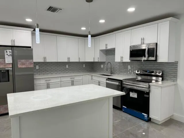 a kitchen with stainless steel appliances a stove a sink a microwave a refrigerator and white cabinets