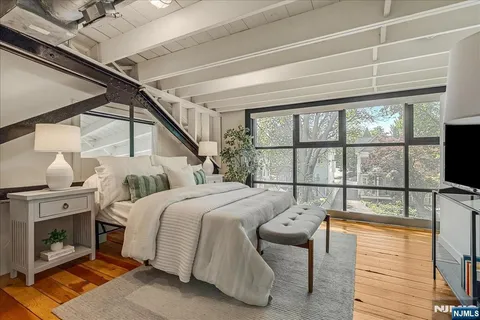 a bedroom with a bed a flat tv screen and a dresser next to a window