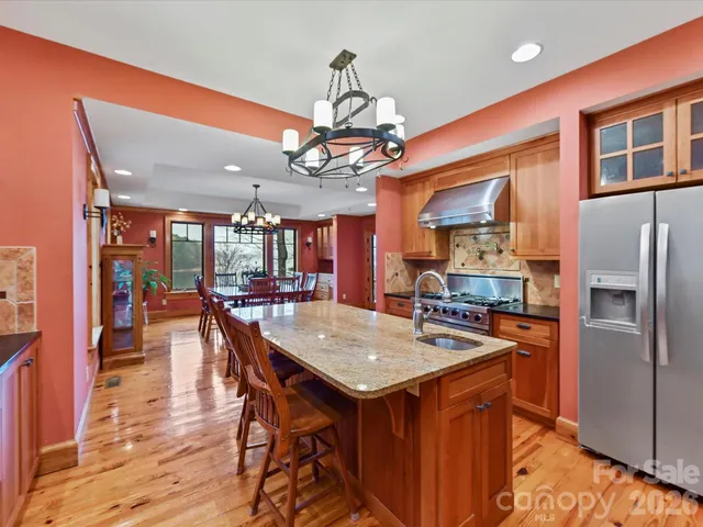 a kitchen with stainless steel appliances granite countertop a kitchen island a stove a refrigerator a oven a dining table and chairs with wooden floor