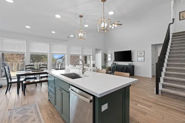 a kitchen with stainless steel appliances a stove top oven a sink dishwasher a dining table and chairs with wooden floor