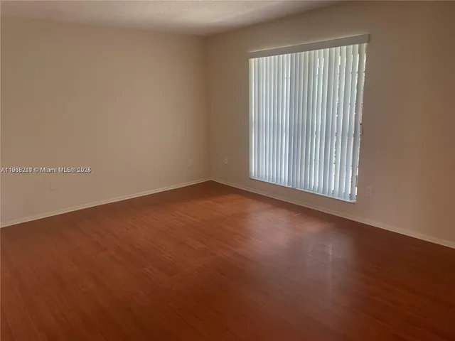an empty room with wooden floor and windows with curtains