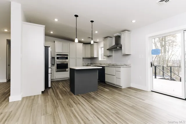 a kitchen with stainless steel appliances kitchen island granite countertop a stove a refrigerator a sink and a oven with wooden floor