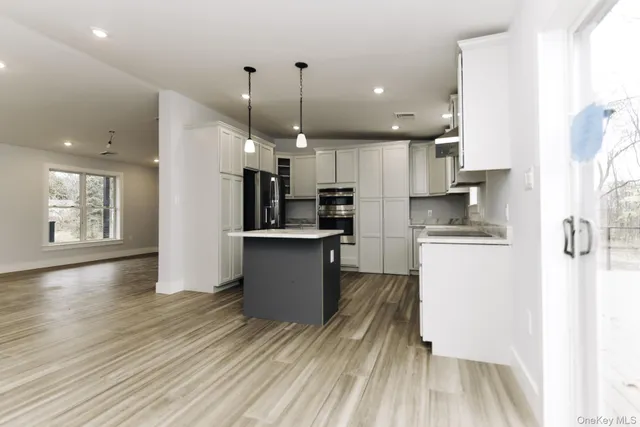 a kitchen with stainless steel appliances kitchen island granite countertop a refrigerator a stove and a wooden floors
