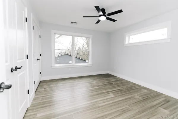 an empty room with wooden floor fan and windows