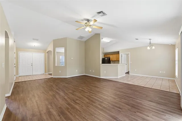 a view of an empty room with wooden floor and a ceiling fan