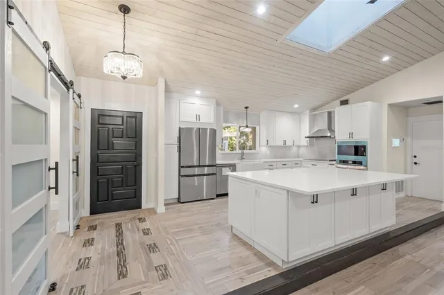 a large white kitchen with stainless steel appliances kitchen island granite countertop a refrigerator a stove a sink dishwasher and white cabinets with wooden floor
