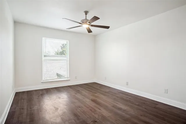 an empty room with wooden floor chandelier fan and windows
