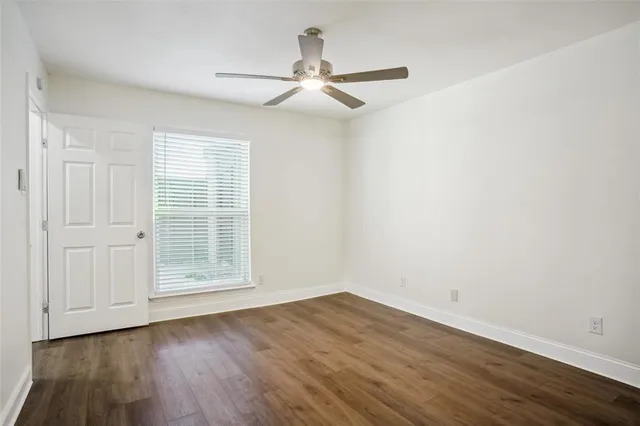 an empty room with wooden floor ceiling fan and windows